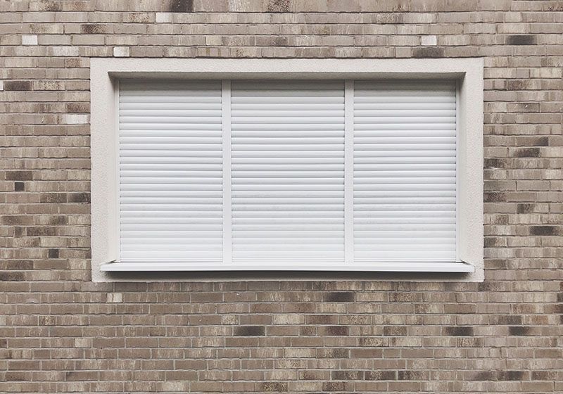 Fachada con una ventana que tiene persianas blancas.