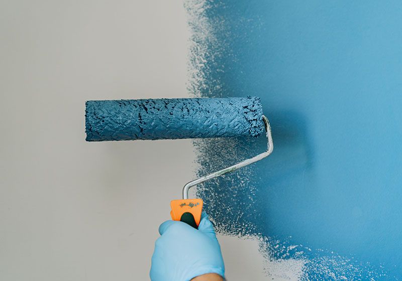 Primer plano de un rodillo que está pintando una pared blanca en azul. Trabajo de pintura.